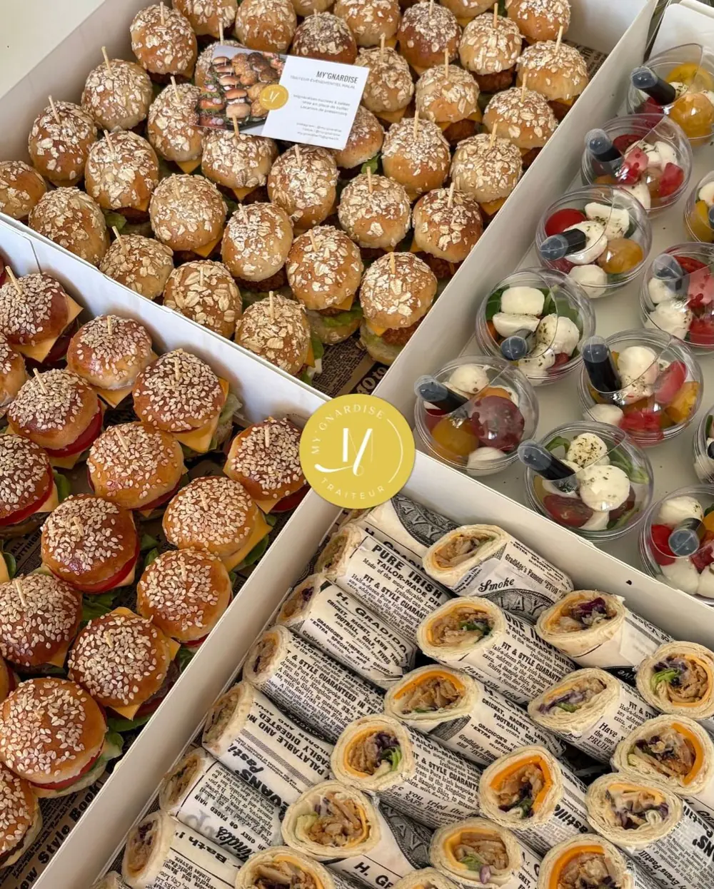 Box ouvertes vues de dessus : mini burgers au sésame, verrines tomate-mozzarella et wraps dans du papier journal