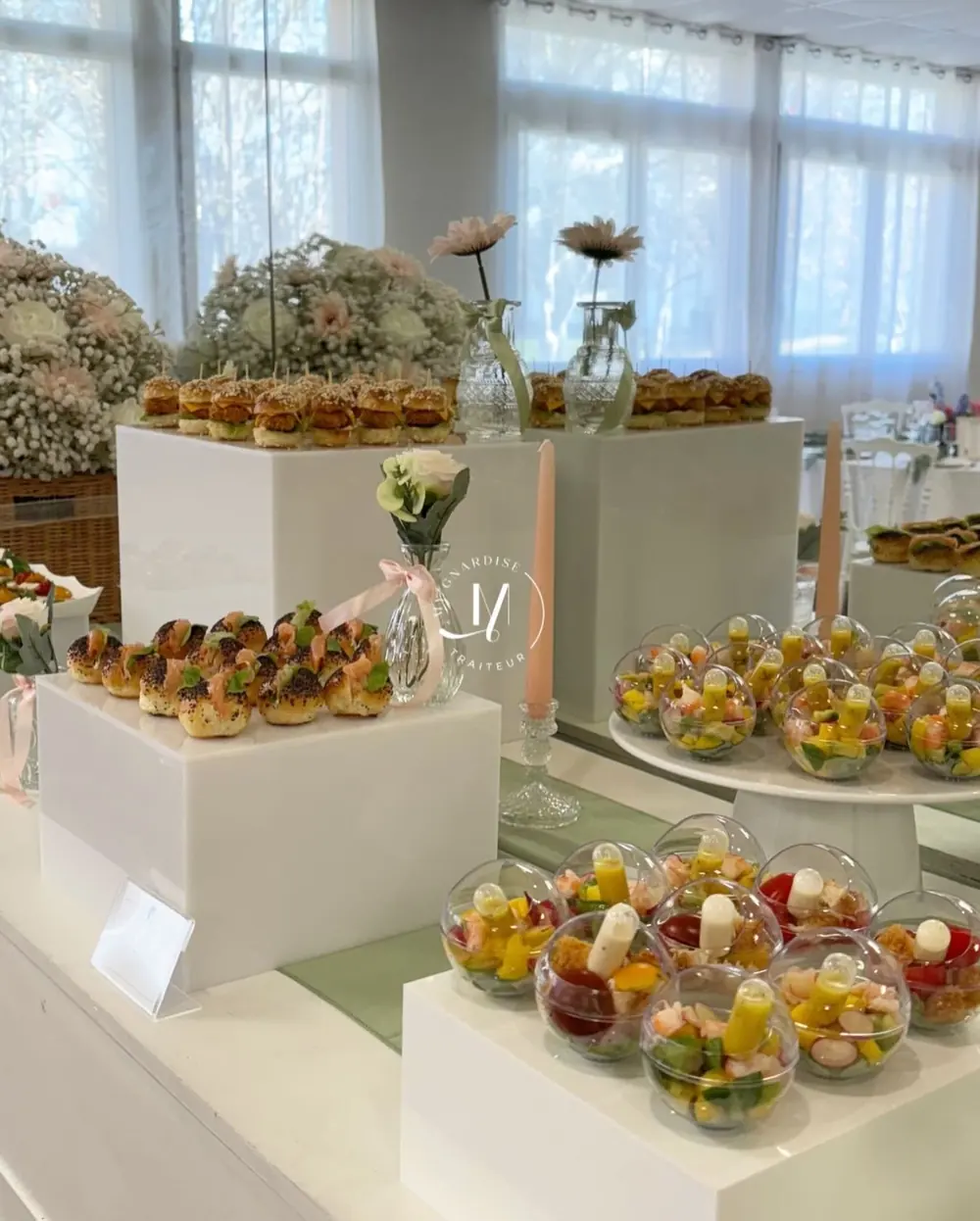 Table dressée avec verrines de salade colorées, navettes au saumon et mini burgers, décor de fleurs pastel